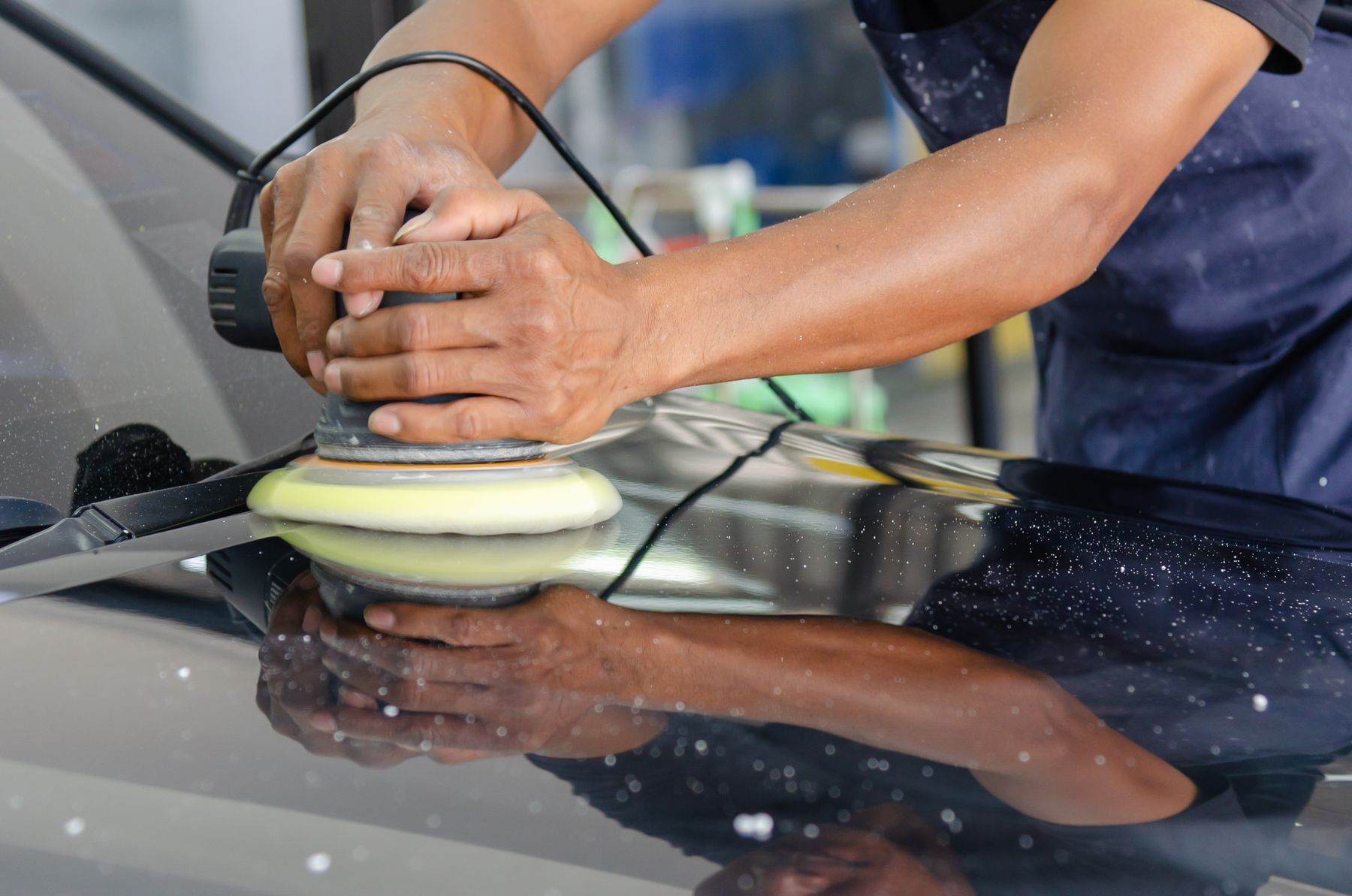 Machine polisher buffing a dark car panel