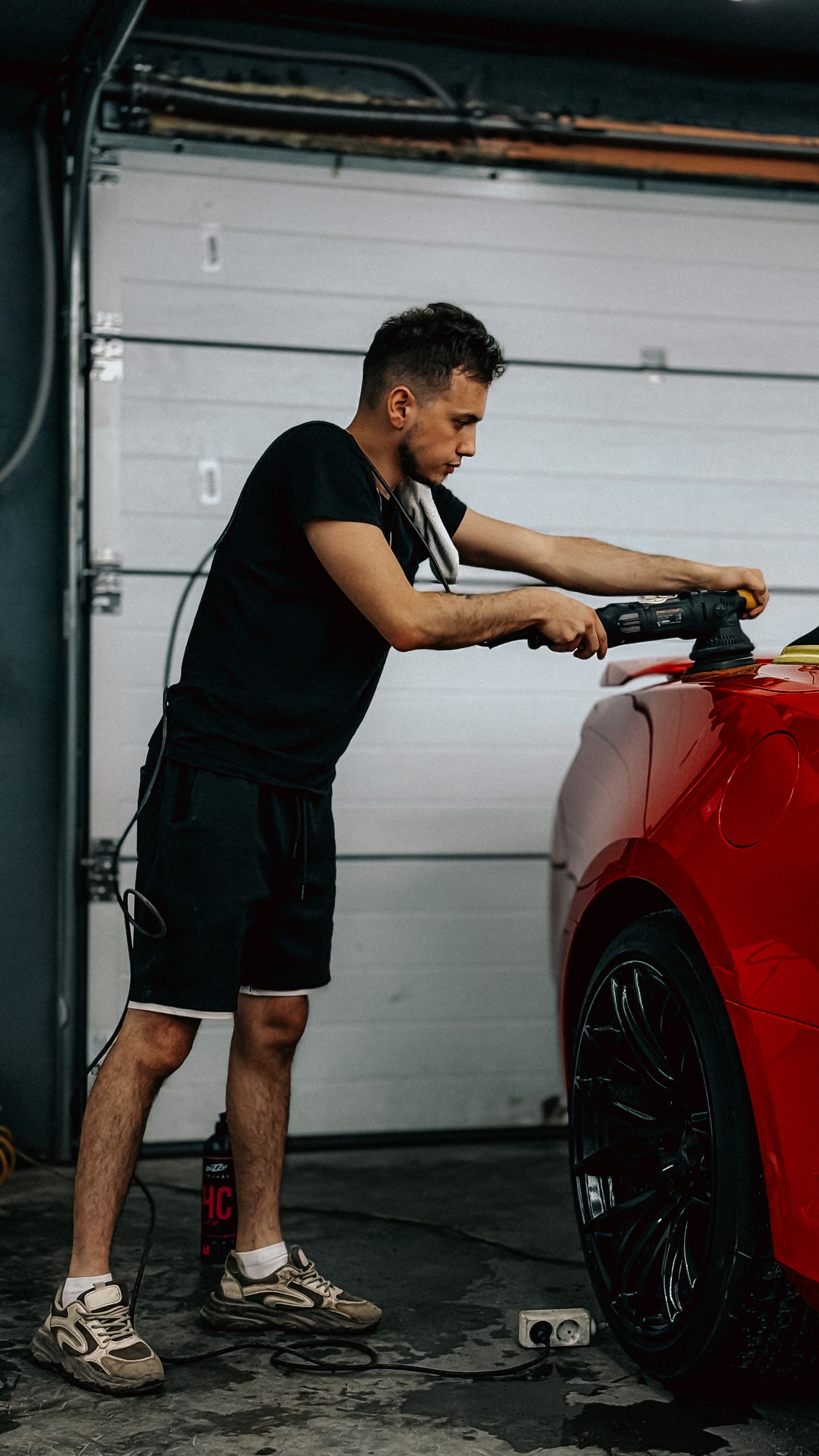 Man polishing a red car in a garage
